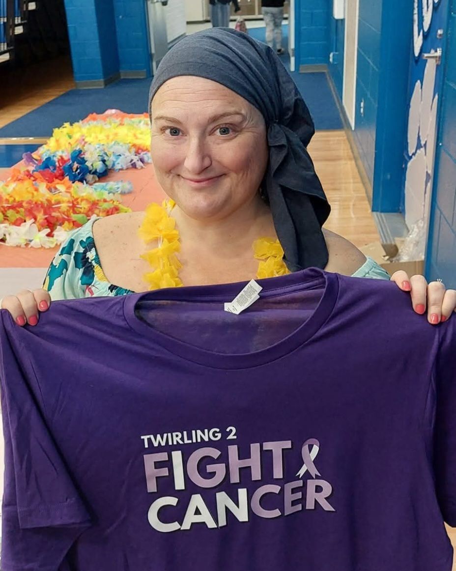 A woman is holding a purple shirt that says fight cancer