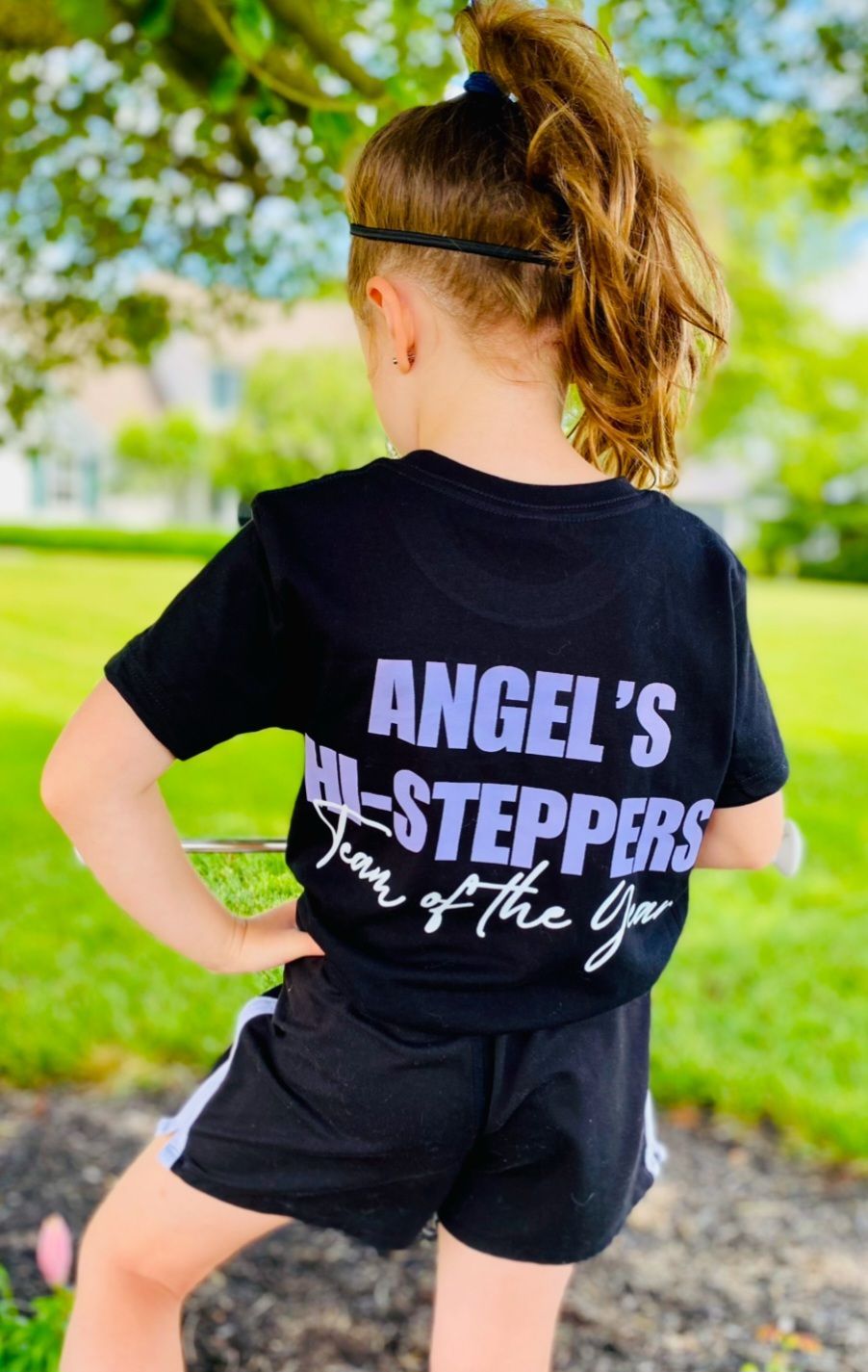 A little girl wearing a black t-shirt and black shorts is standing in a park.