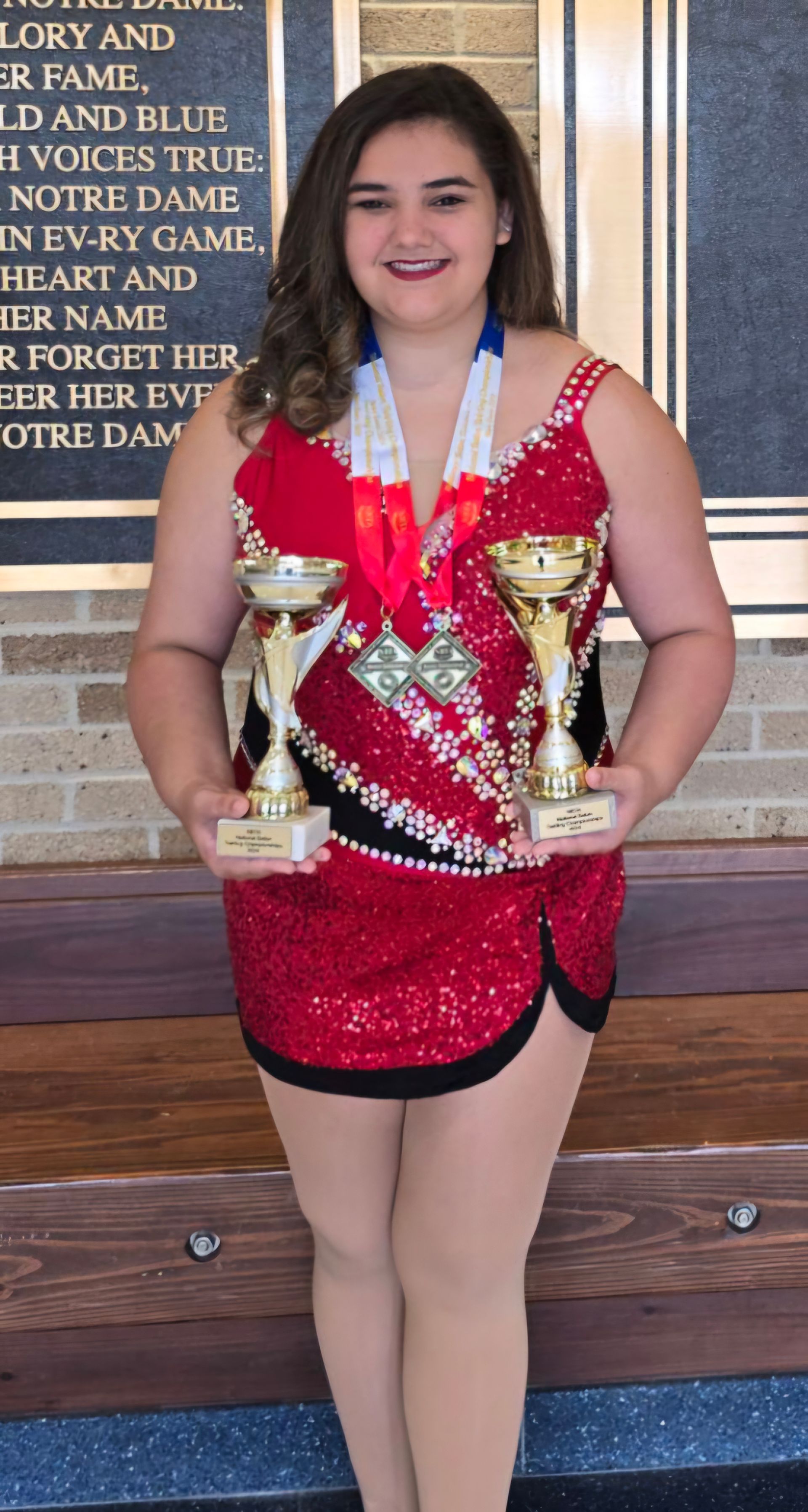 A woman in a red dress is holding two trophies.