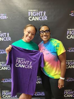 Two women are standing next to each other holding a purple shirt that says `` fight cancer ''.