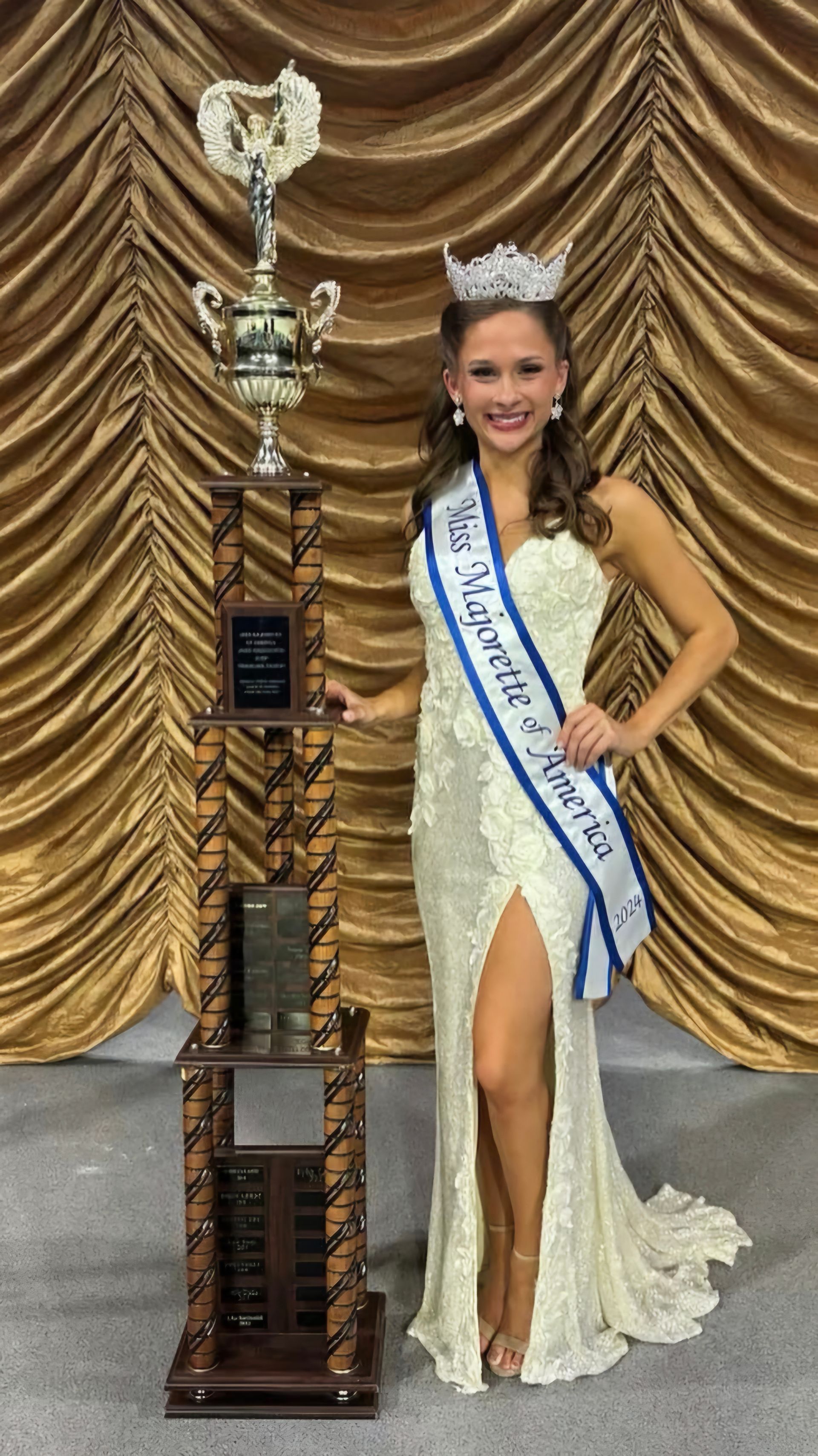 A woman in a white dress is standing next to a trophy.