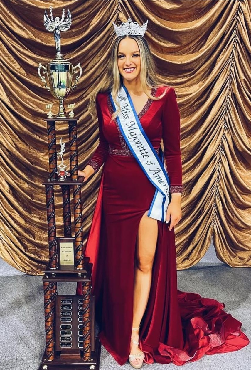 A woman in a red dress is standing next to a trophy