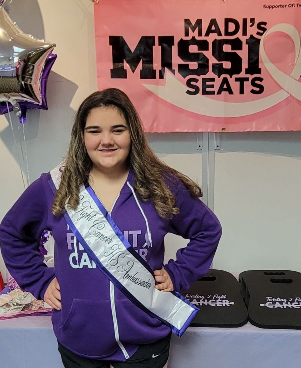 A girl is standing in front of a sign that says madi 's mission seats.