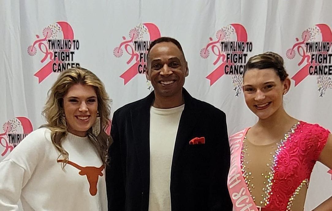 A man and two women are posing for a picture in front of a pink curtain.