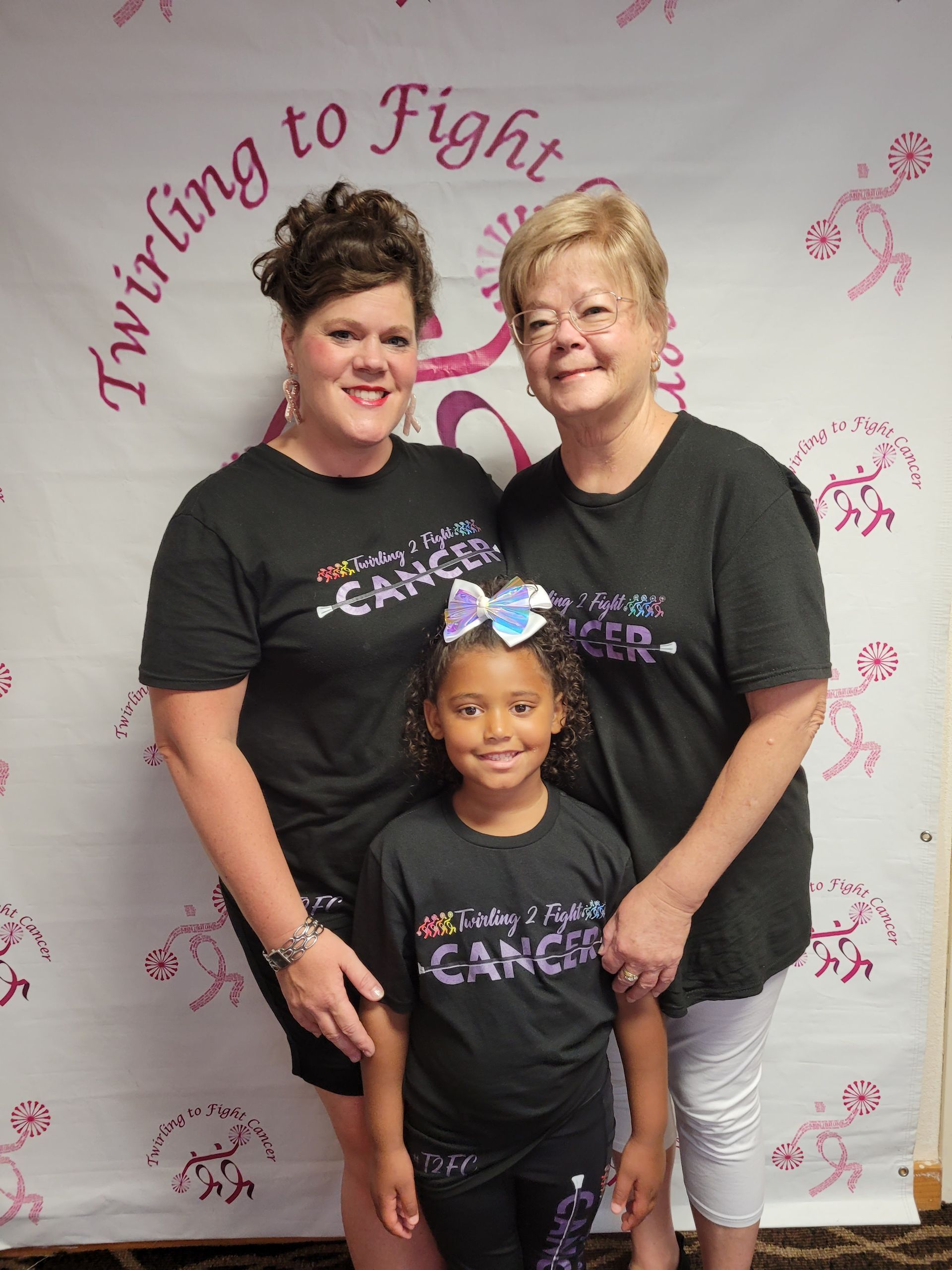 Three women and a little girl are posing for a picture in front of a banner that says ' twirling to fight cancer '