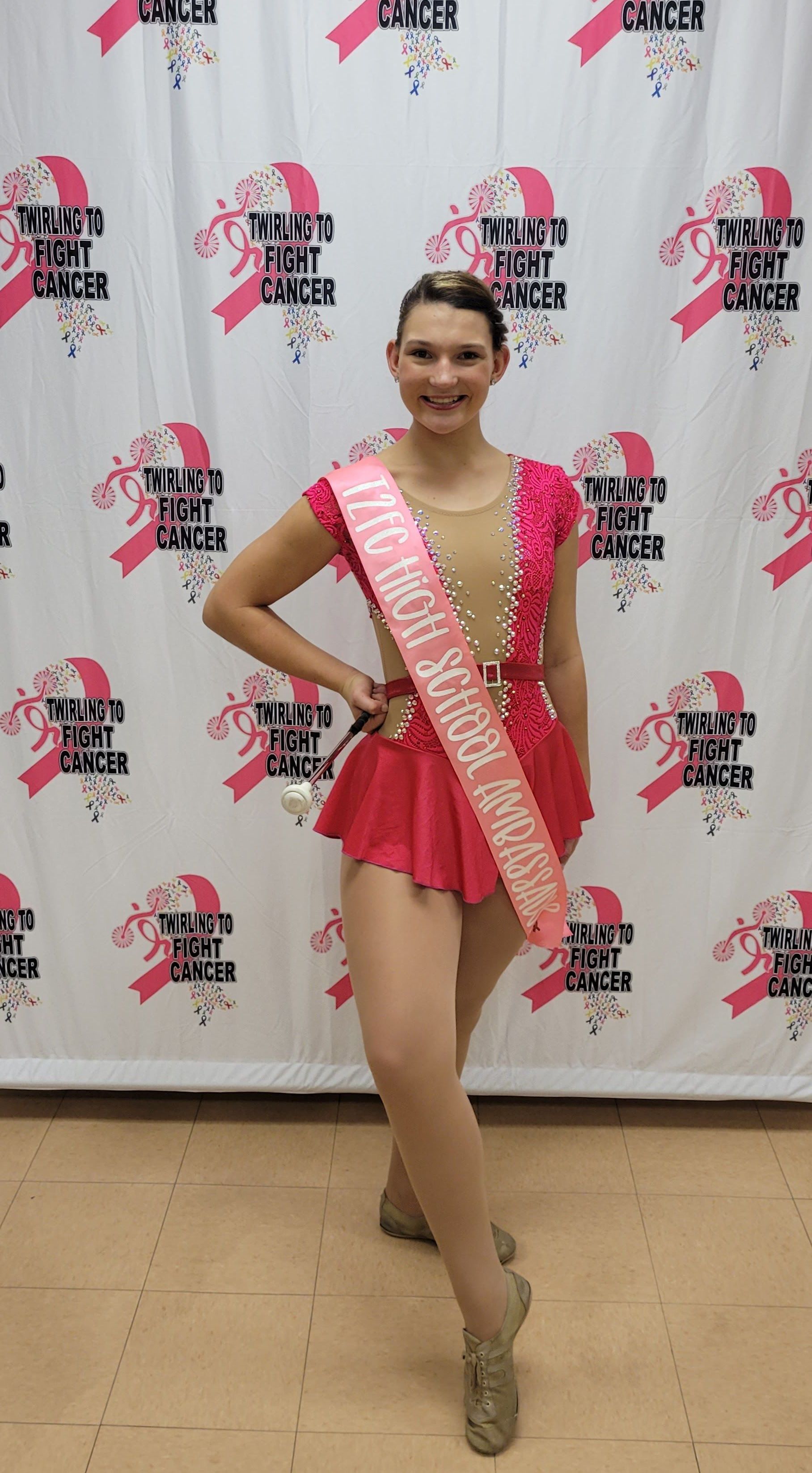 A woman in a pink dress is standing in front of a breast cancer awareness backdrop.