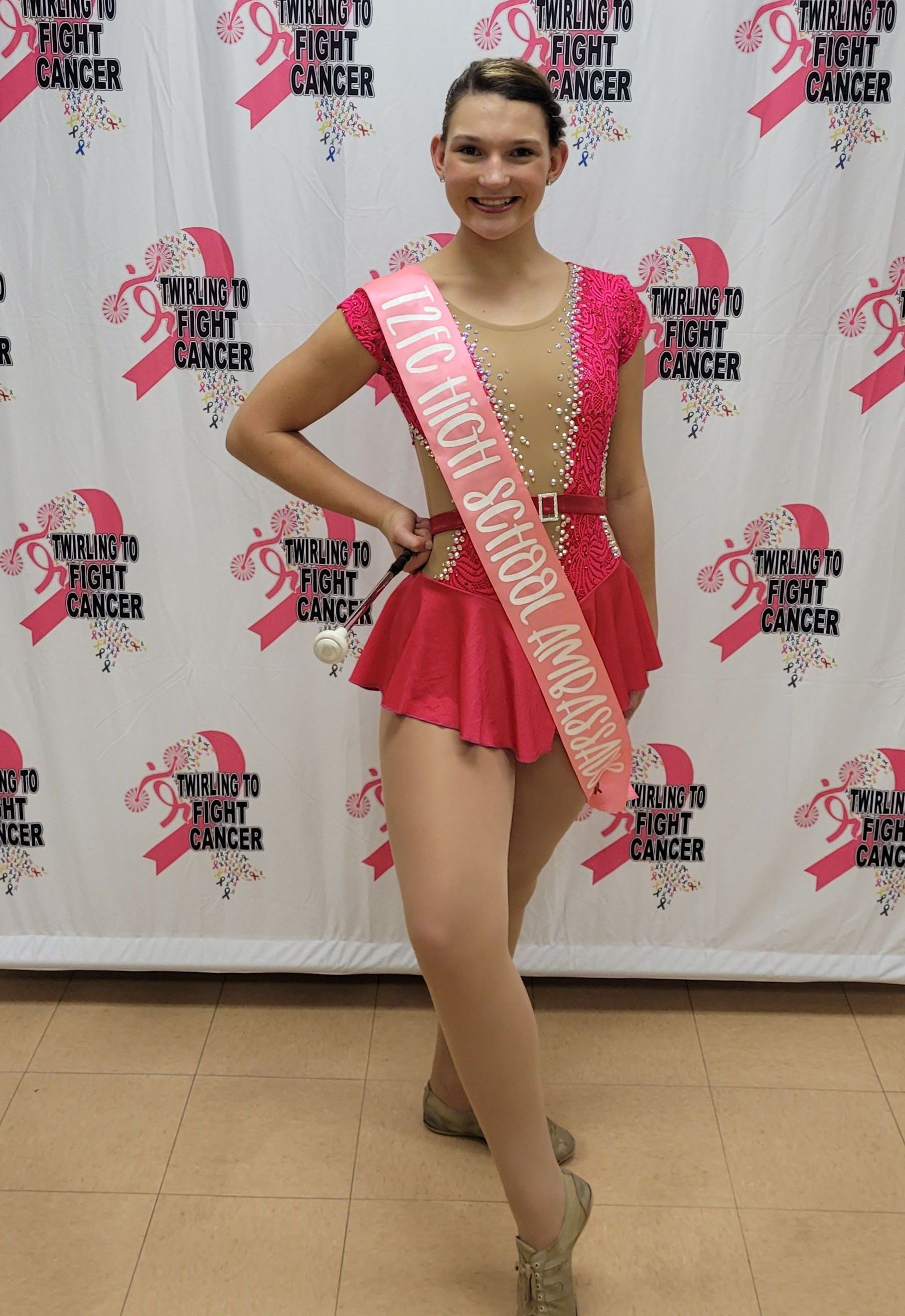 A woman in a pink dress is standing in front of a breast cancer awareness backdrop.