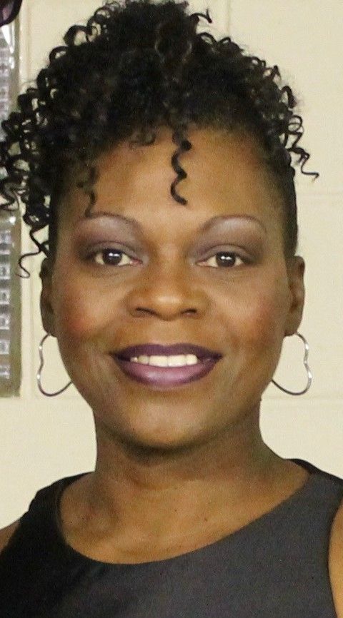 A woman with curly hair and purple lipstick is smiling for the camera.