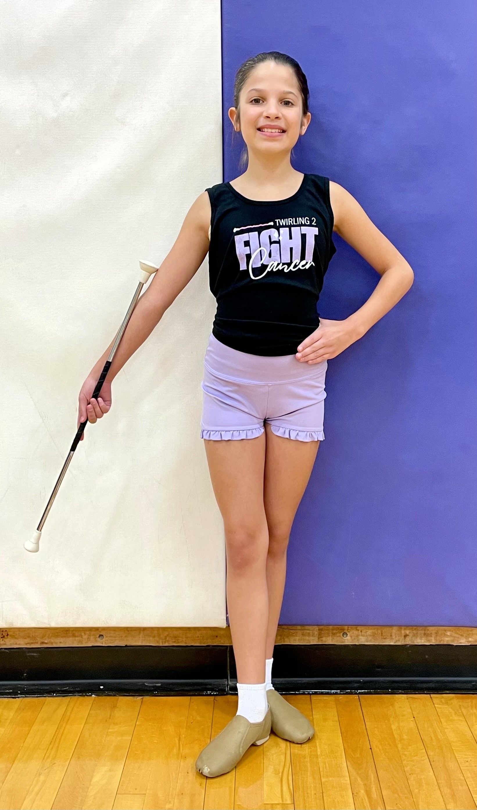 A person in athletic wear holding a baton, standing against a blue and white wall.