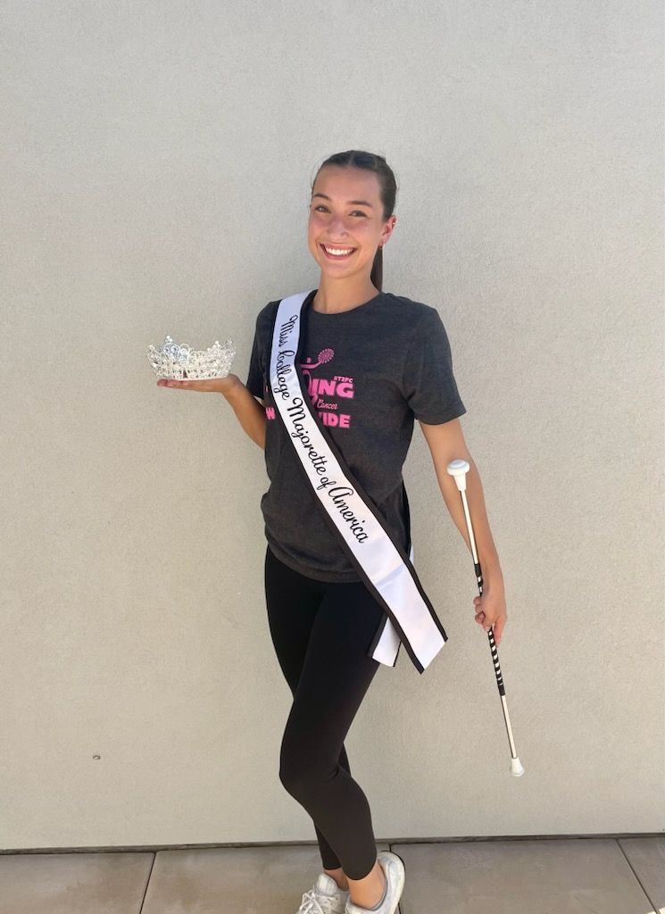 A woman wearing a sash and holding a crown and baton