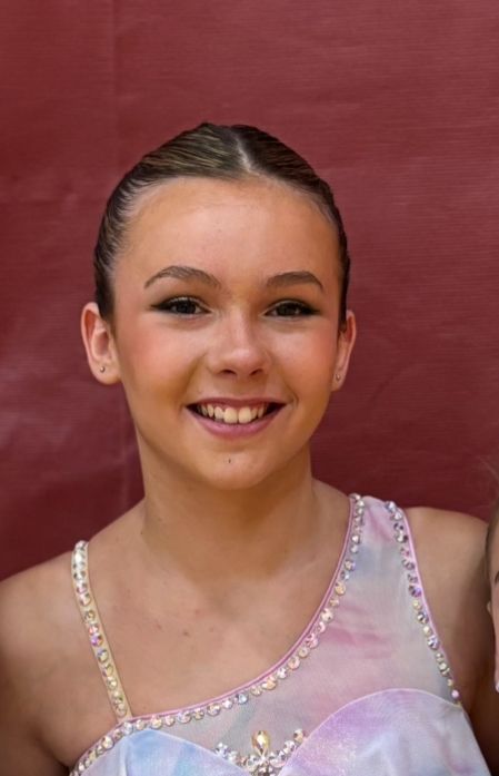 Young person smiling, wearing a sparkly costume, in front of a red background.
