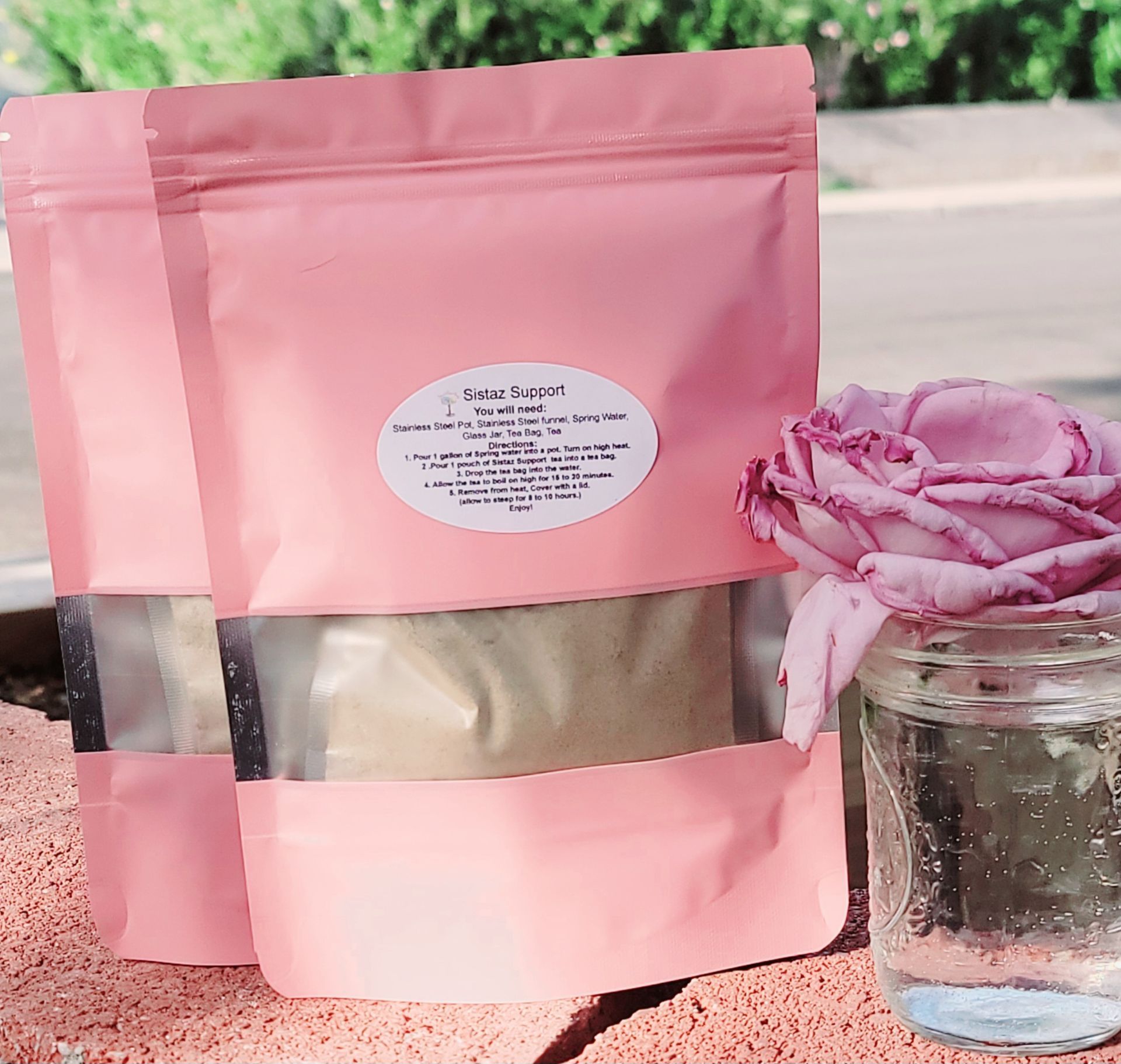 Two pink bags of facial mask next to a rose in a jar.