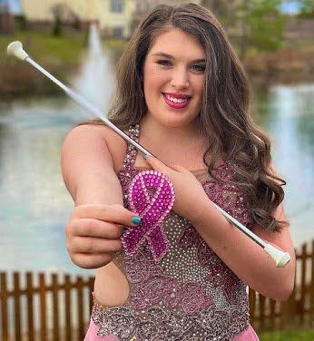 A woman in a pink dress is holding a baton with a pink ribbon on it.