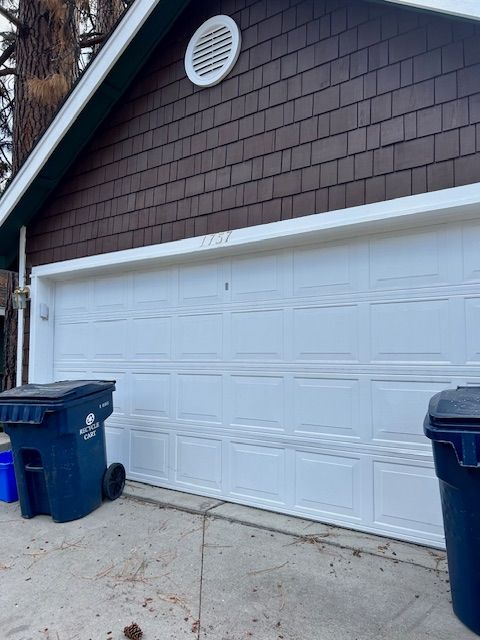 Two blue garbage cans are parked in front of a garage door