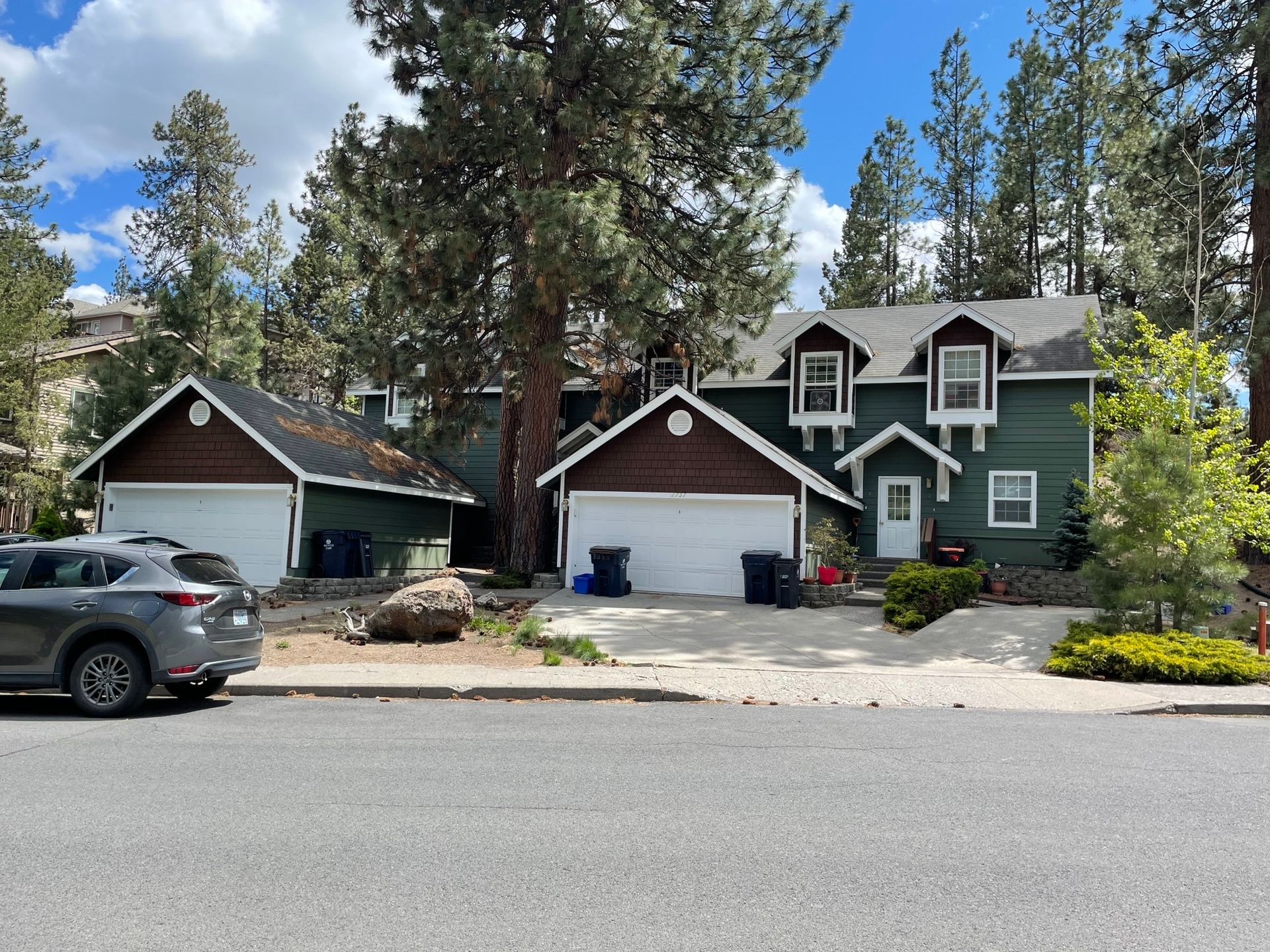 A car is parked in front of a green and brown house.