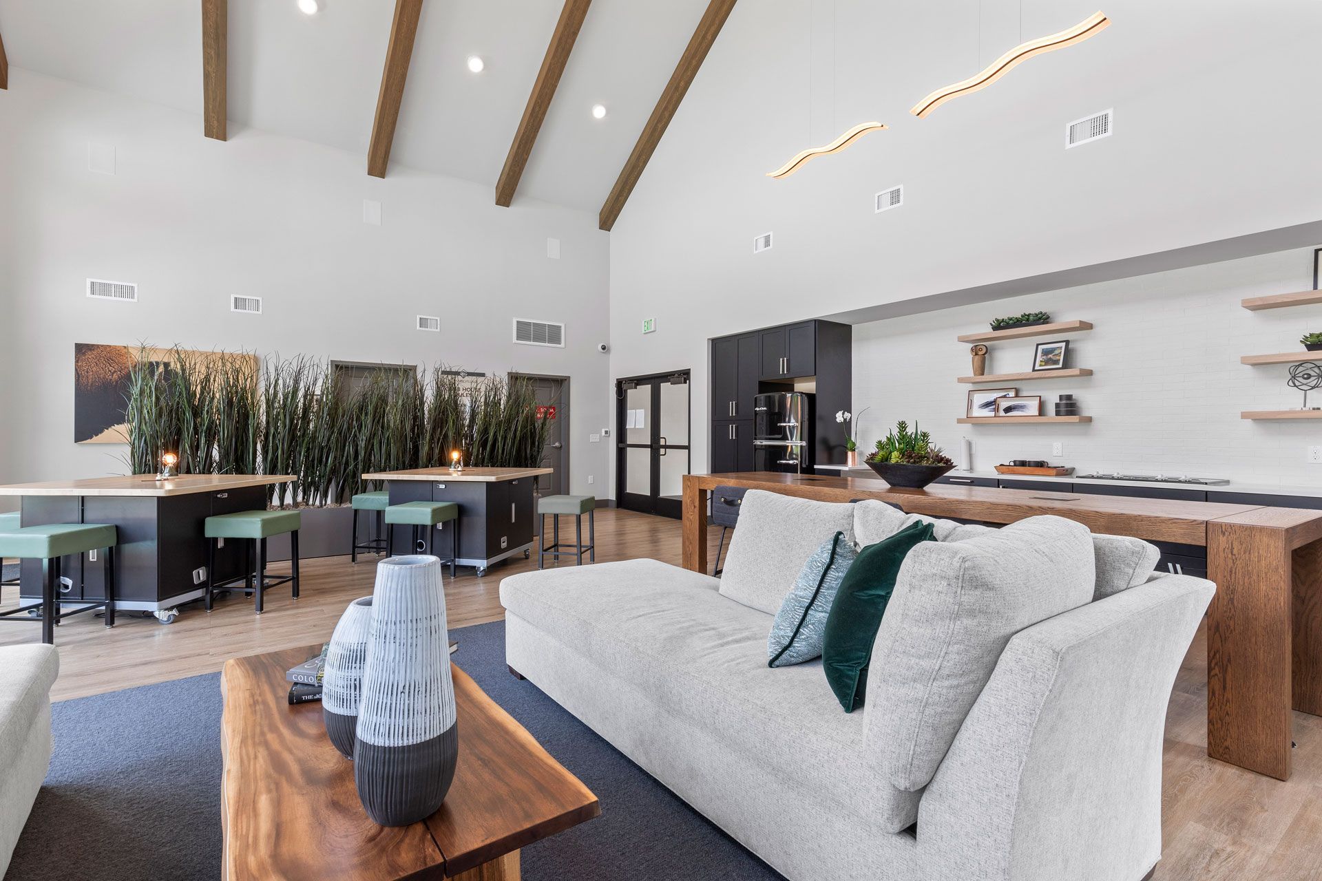 Modern lounge with high vaulted ceilings, cozy textured sofa, wooden coffee table, and communal tables with stools.