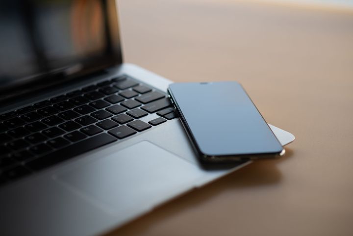 A silver smartphone resting on the keyboard and trackpad area of an open silver laptop on a light brown surface.