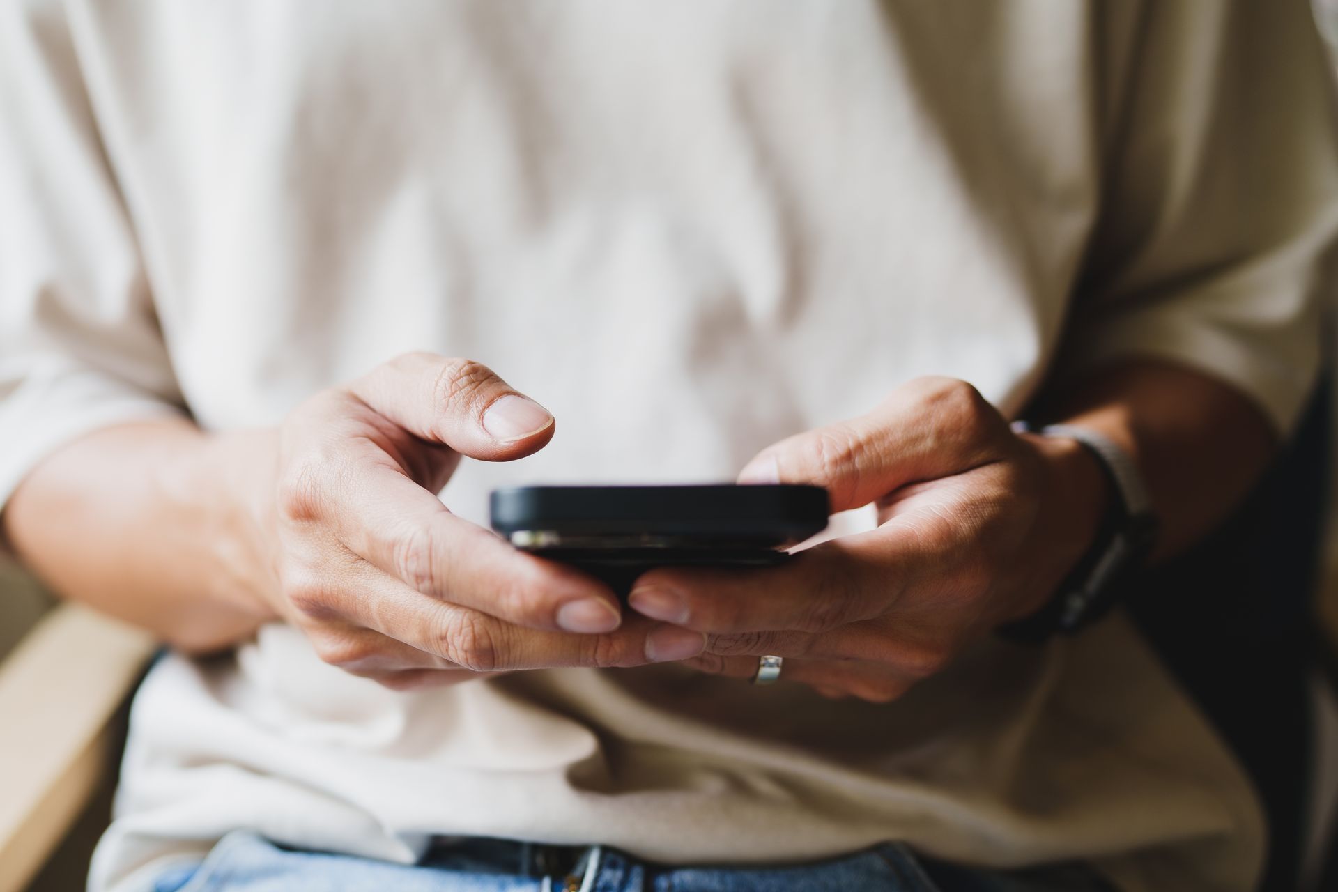 A close-up of a person in a beige shirt holding a smartphone in both hands.