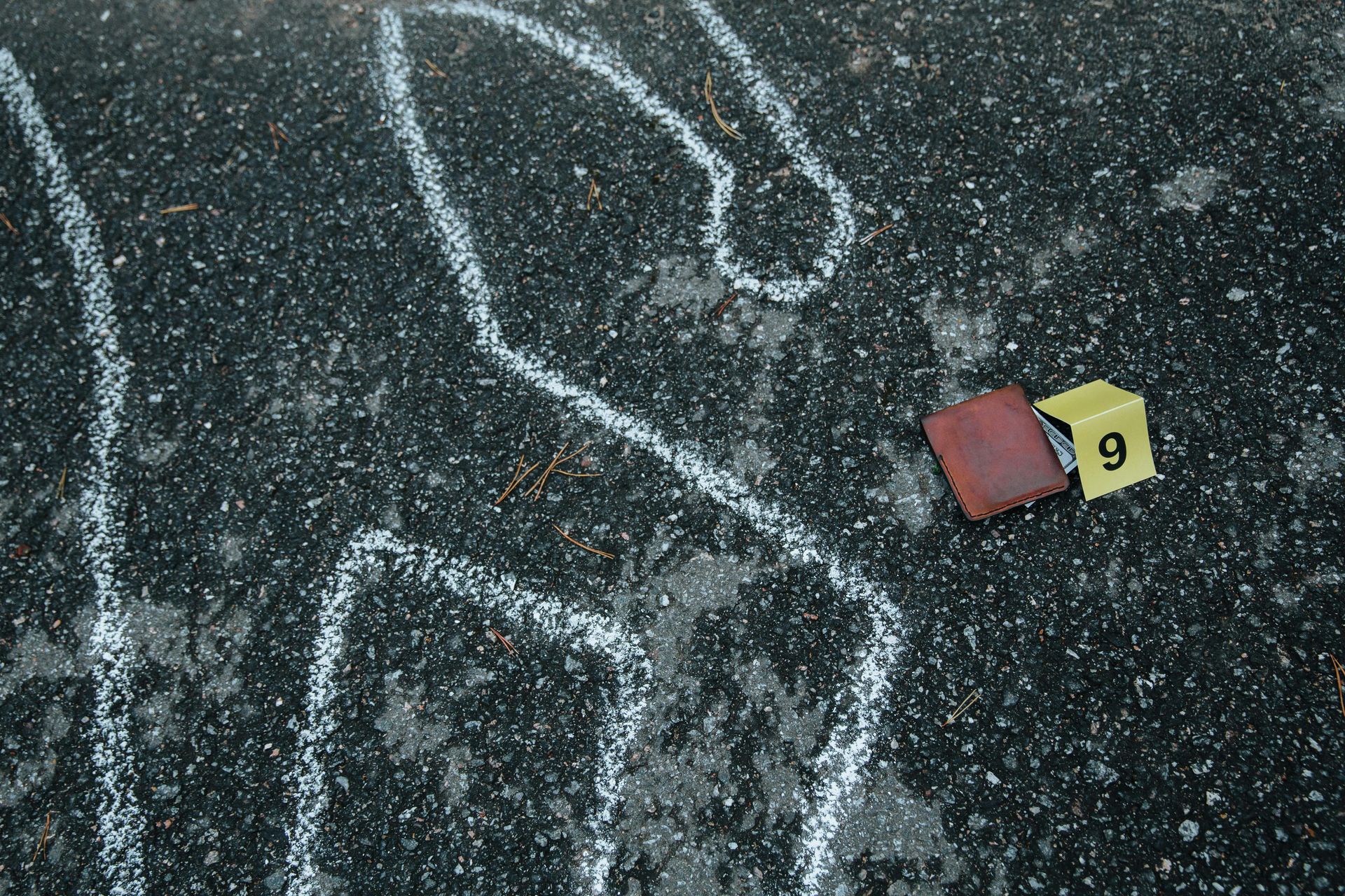 Chalk outline on pavement with evidence markers at a crime scene.