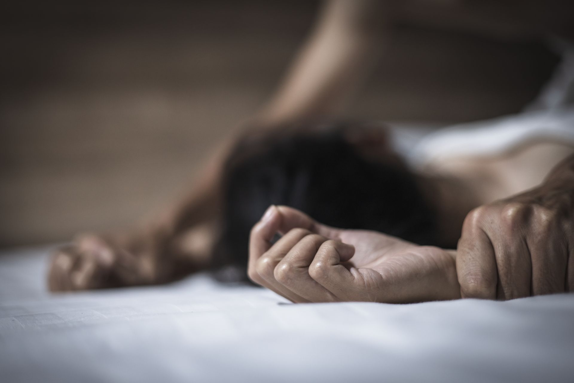 Person's arm over another person's body on a bed, potentially involved in sexual activity, with a dimly lit setting.