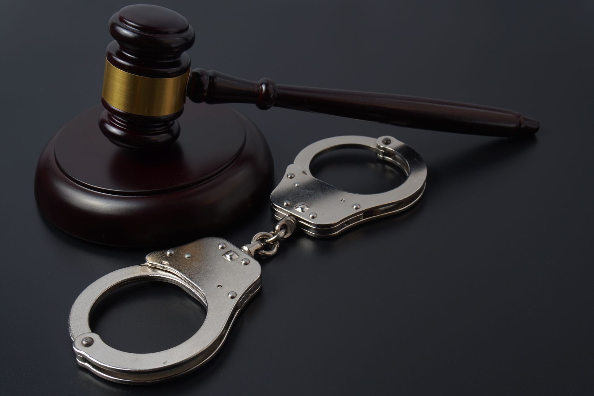 Gavel and handcuffs on black surface, representing law and justice.
