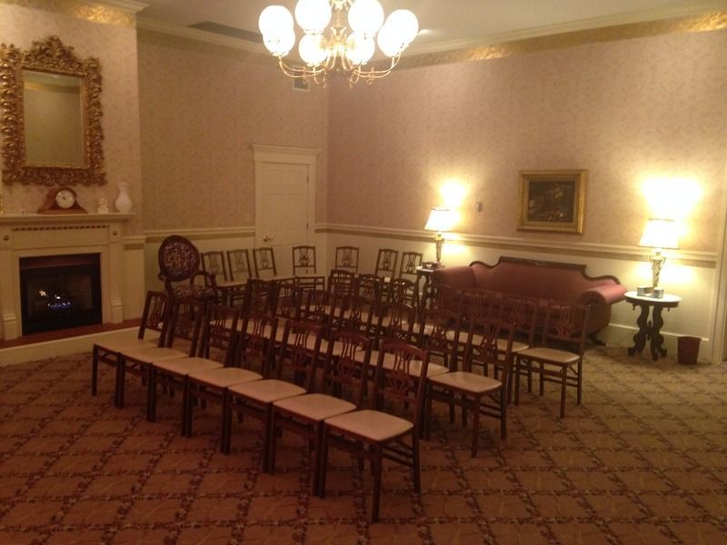 Formal room with rows of chairs, fireplace, sofa, and chandelier.