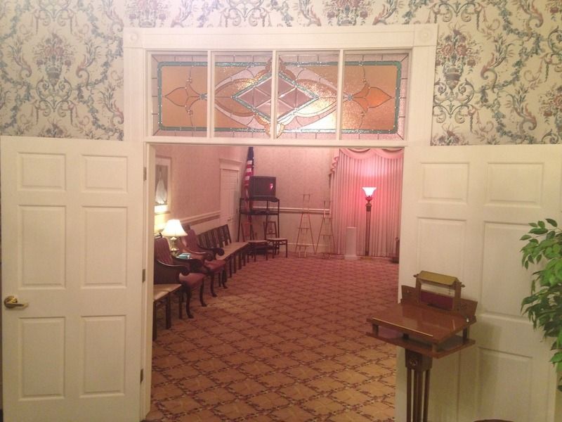 Interior view of a room with open doors, stained glass, patterned wallpaper, and seating.