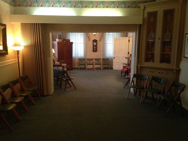 Interior of a room with chairs, a clock, a cabinet, and a doorway. Lighting is soft.