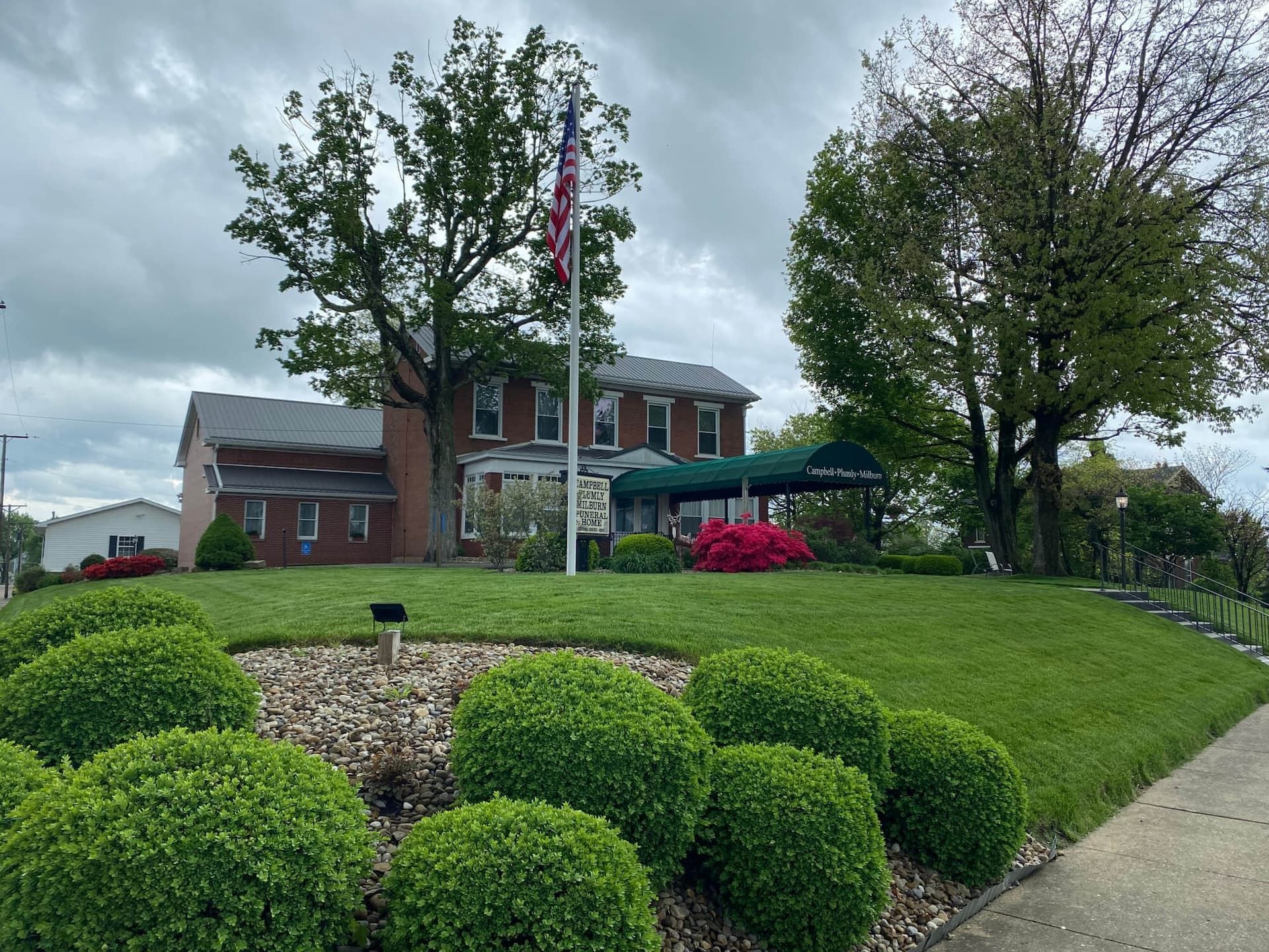Green lawn with trimmed bushes in front of a brick building with an American flag.