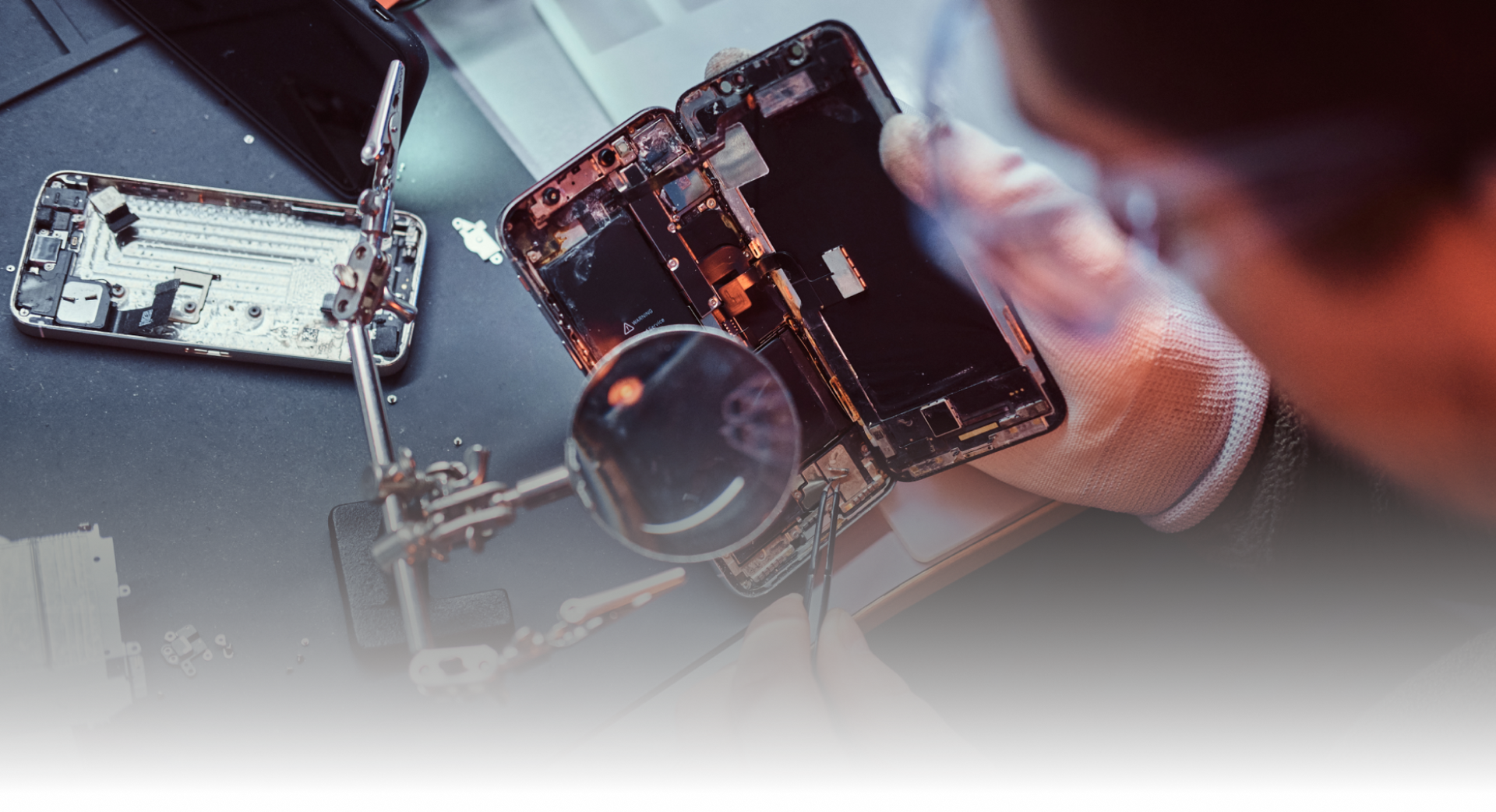 A man is working on a cell phone with a magnifying glass.