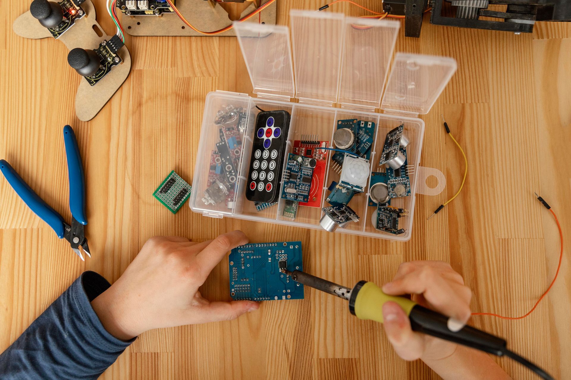 A person is soldering a piece of electronic equipment on a wooden table.