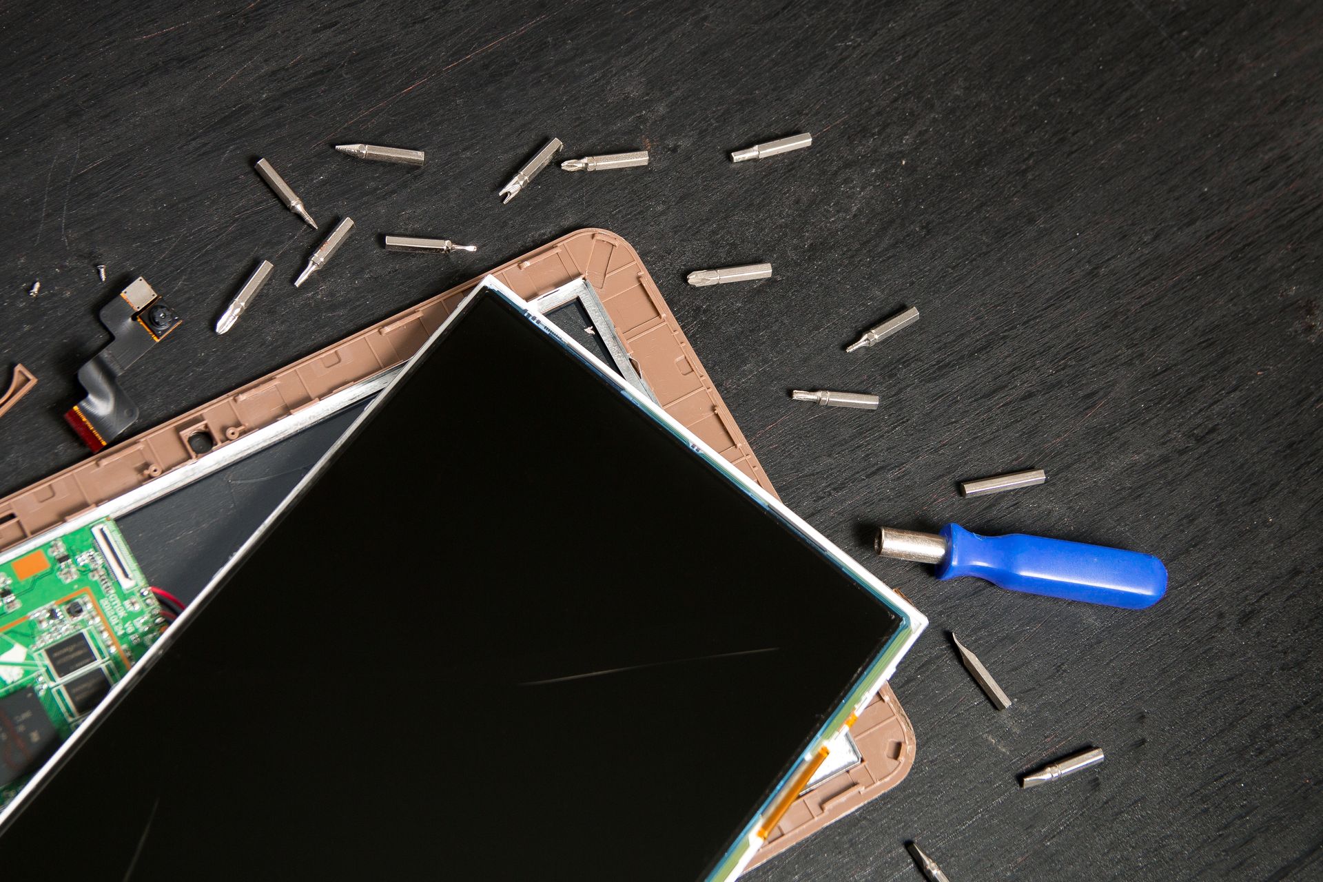 A tablet is being repaired on a table with screws and a screwdriver.