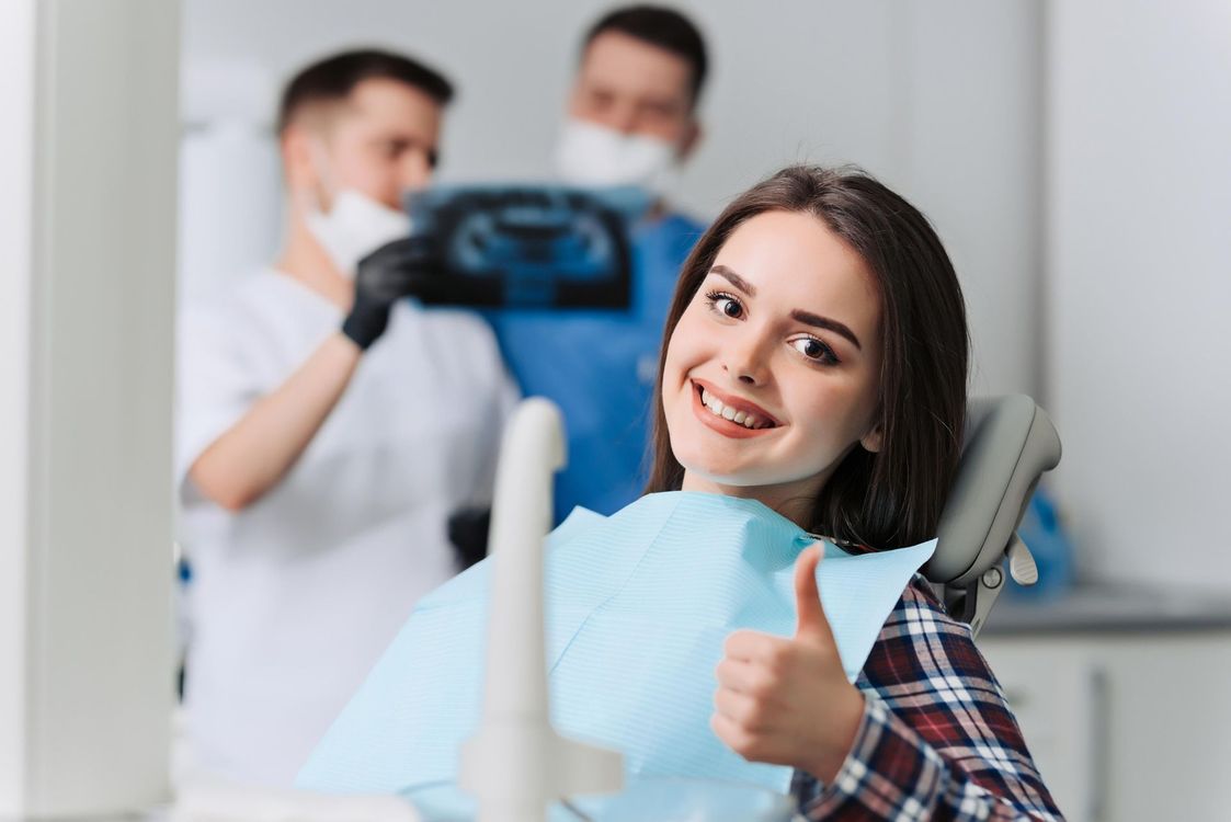 A woman is giving a thumbs up while sitting in a dental chair.