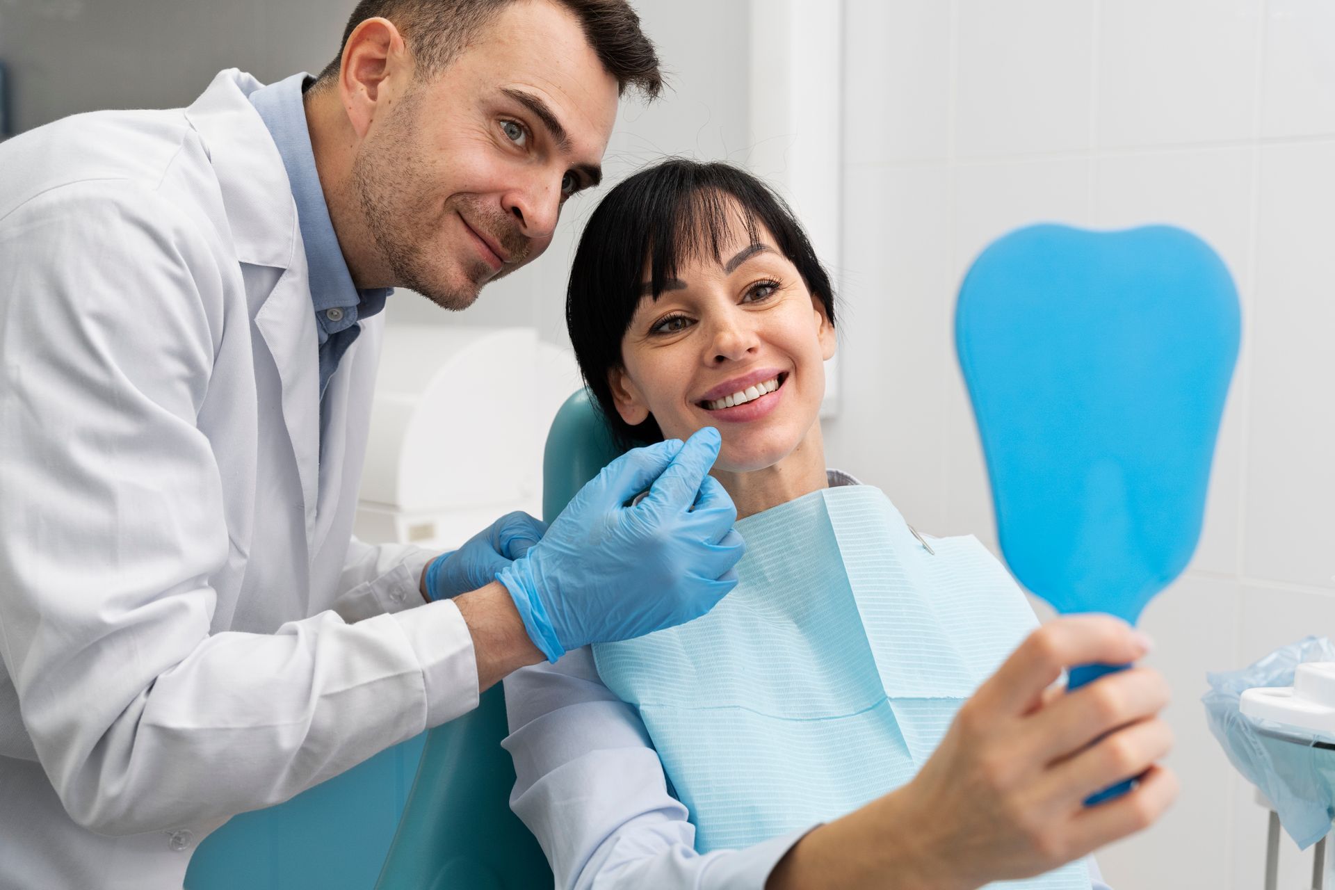 A woman is sitting in a dental chair looking at her smile in a mirror.