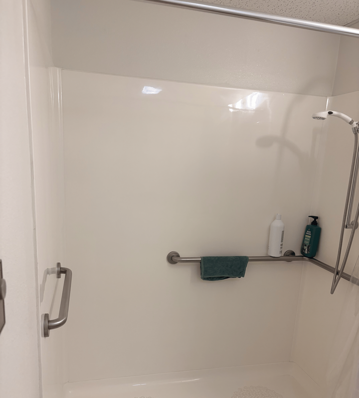 Walk-in shower with a grab bar, handheld showerhead, and wall-mounted toiletries