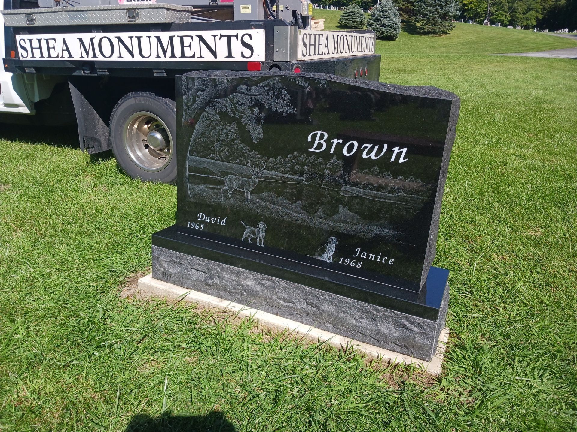 Black granite headstone with etched scene, Brown surname, and names/dates; set on stone base.