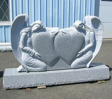 Gray granite memorial with two kneeling angel figures embracing connected heart shapes.