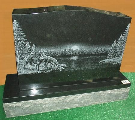 Black granite headstone with etched deer scene by water at sunset.