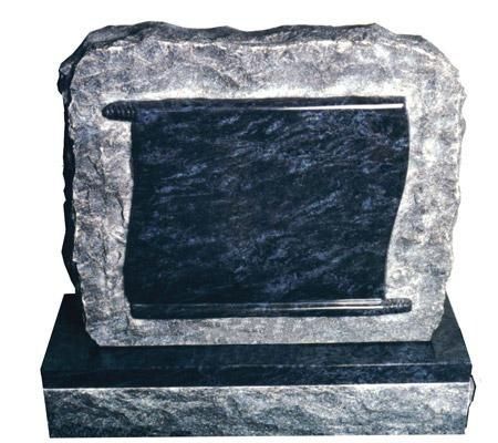 Dark stone headstone with a central dark rectangle, surrounded by rough-cut stone, resting on a base.