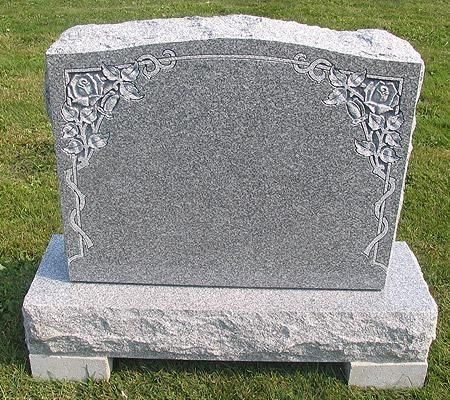 Gray granite headstone with floral carving, set on a matching base in grassy area.