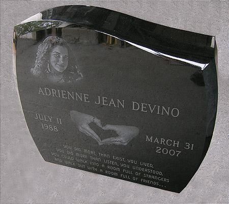 Black granite headstone with a woman's portrait, name, birth/death dates, hand-heart symbol, and inscription.