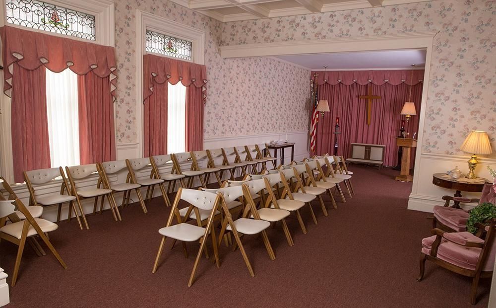 Interior of a funeral home with rows of chairs, curtains, and a cross.
