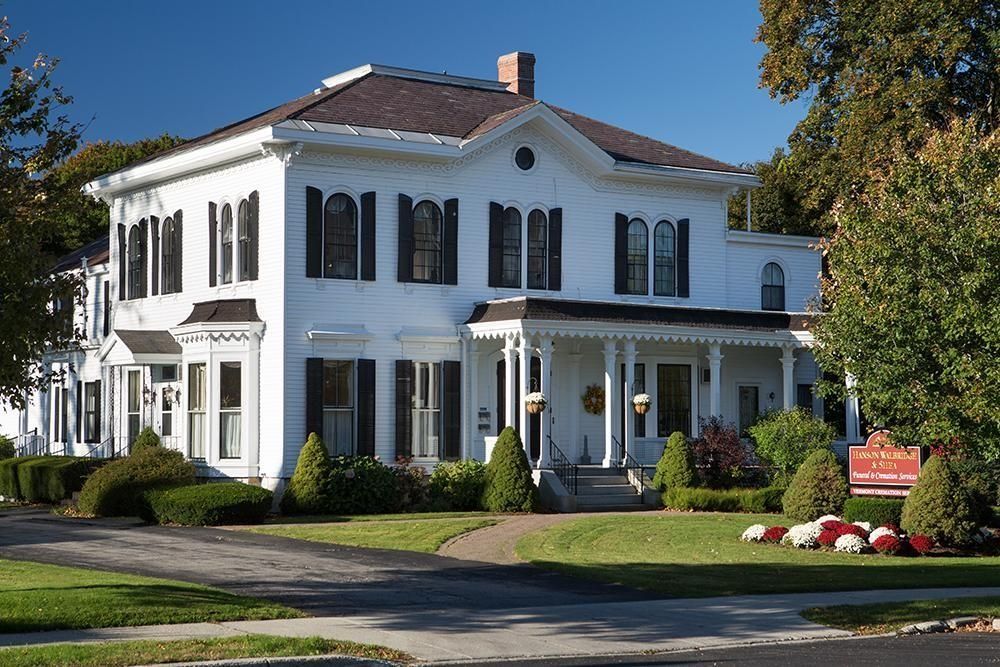 White two-story house with black shutters, porch, and a well-manicured lawn.