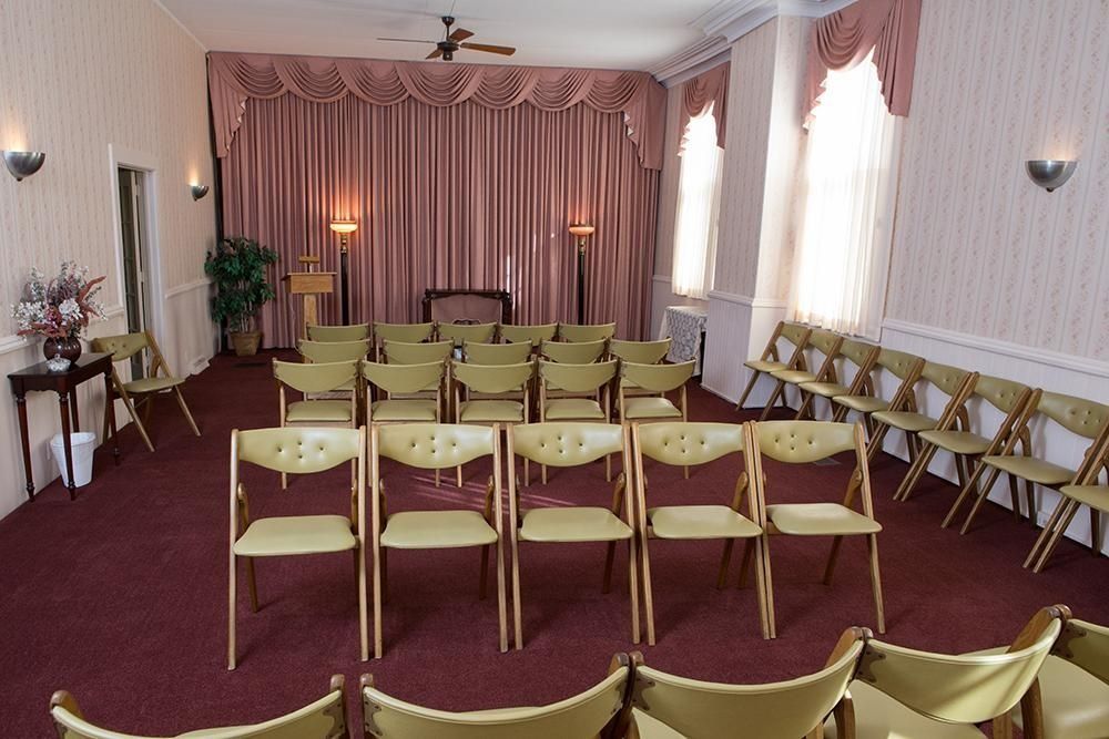 Interior of a funeral home chapel with rows of chairs, red carpet, and pink curtains.