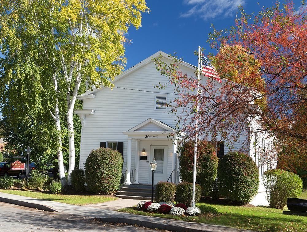 White building with shrubs, trees with yellow and red leaves, American flag.