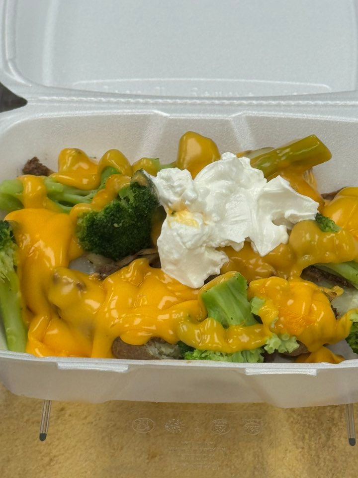 Steak and broccoli dish in a to-go container, covered in melted orange cheese and a dollop of white sour cream.