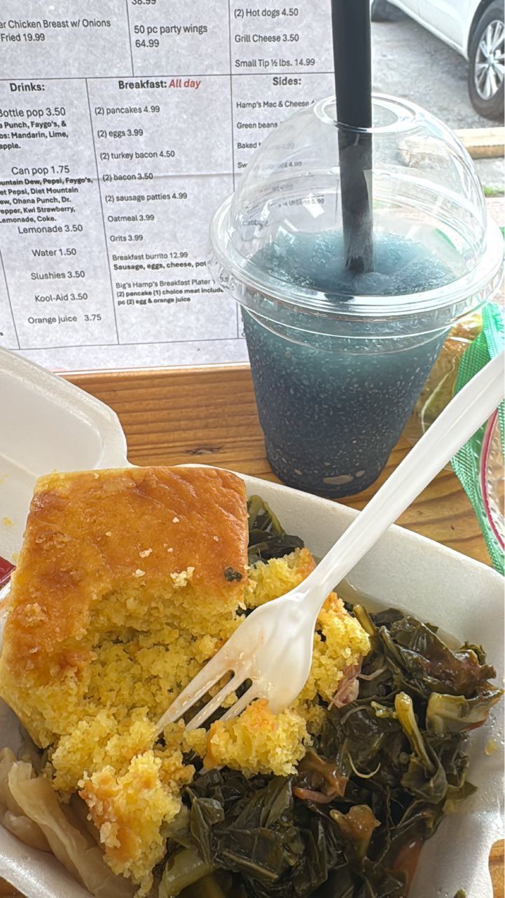 A tray with cornbread, collard greens, and a blue slushie with a straw. A menu is in the background.