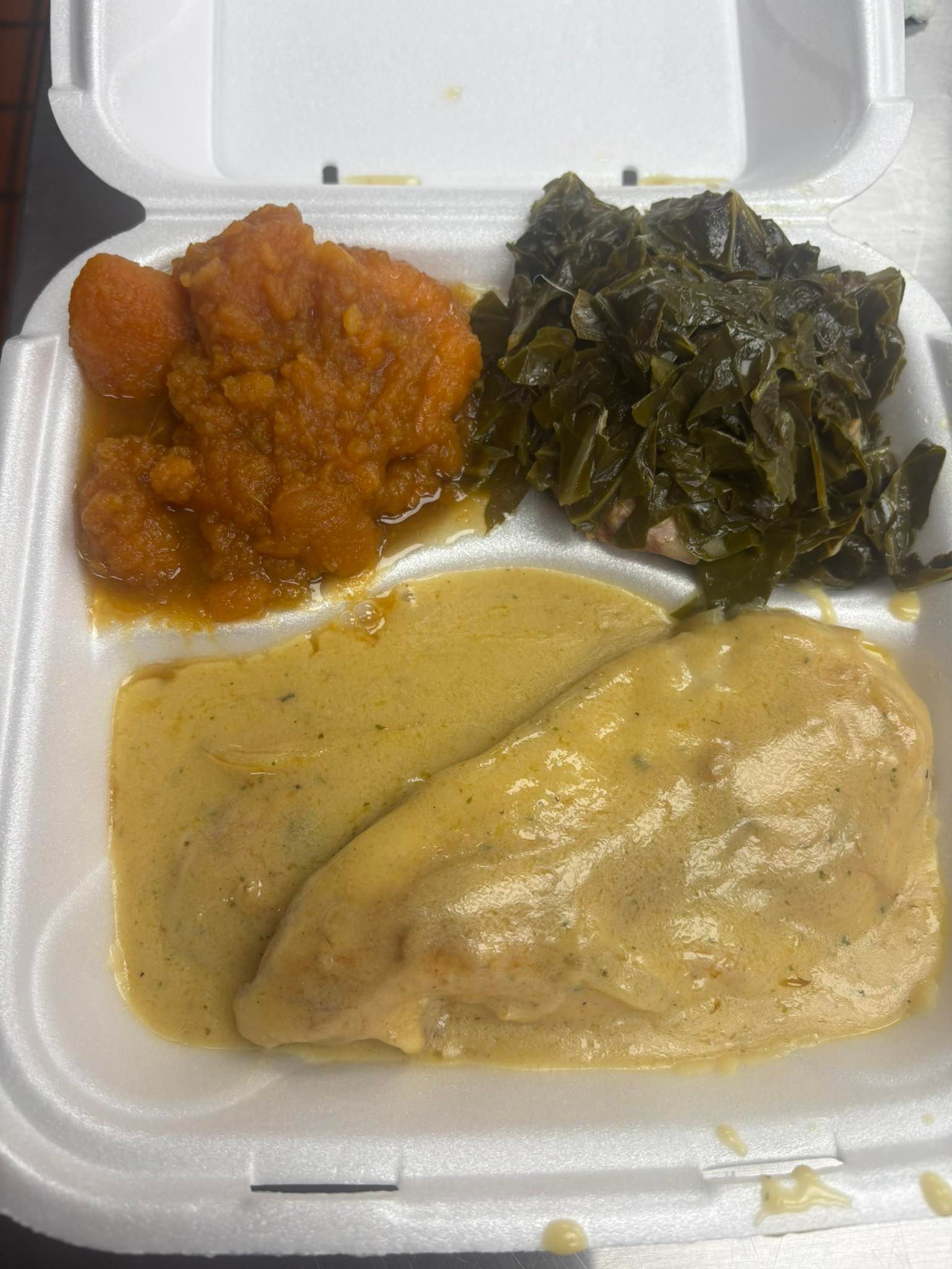 Meal in a white container: mashed sweet potatoes, collard greens, and chicken covered in gravy.