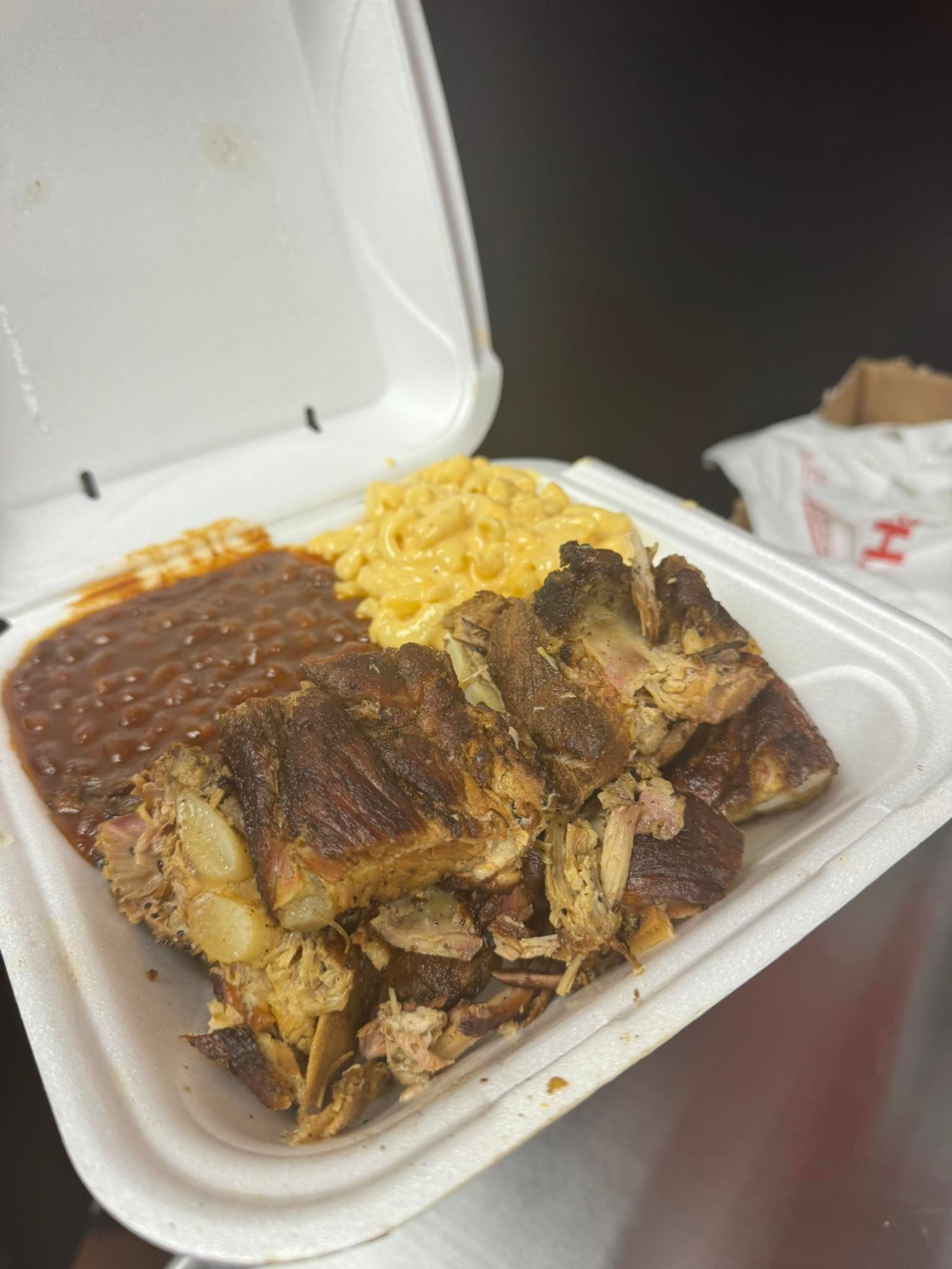 Barbecue takeout meal in a white foam container. Includes ribs, mac and cheese, and baked beans.