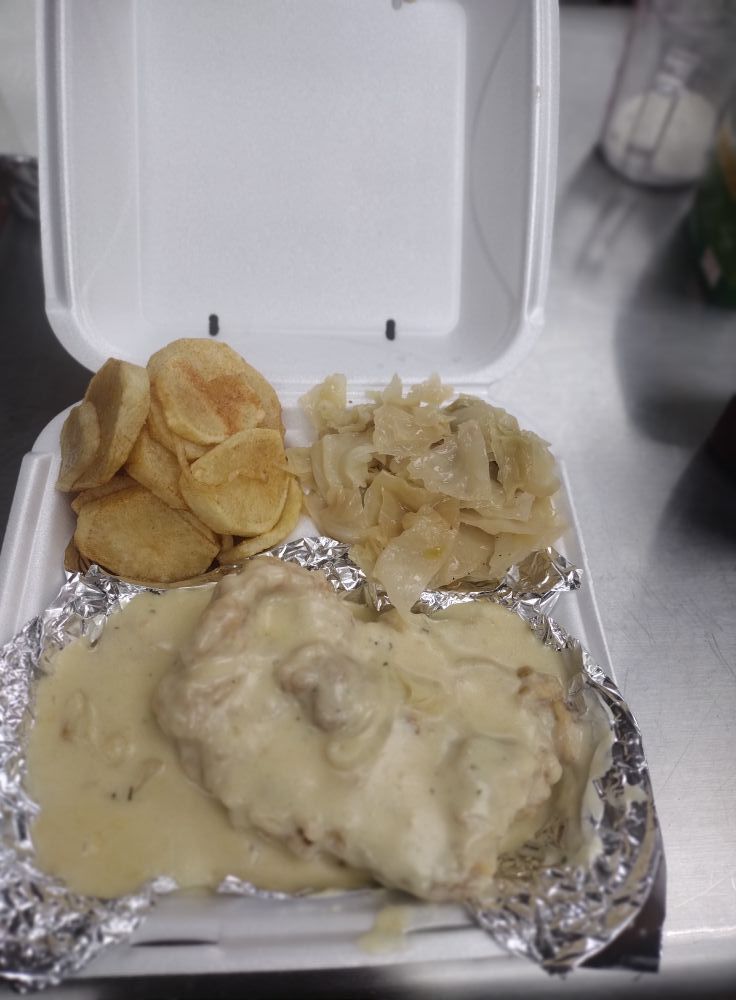 Chicken fried steak with gravy, apples, and cabbage in a styrofoam takeout container.